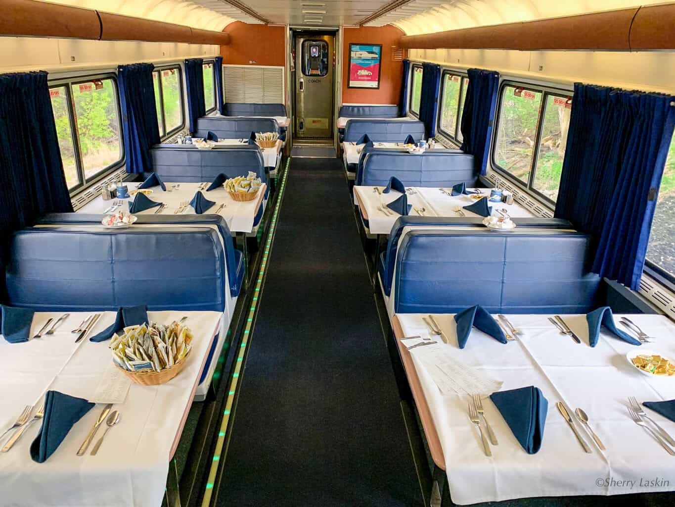 Amtrak dining car with blue seating benches and white tablecloths.