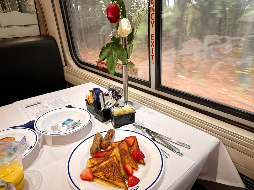 Amtrak dining car at breakfast with French Toast and strawberries. A vase with two roses is on the table.